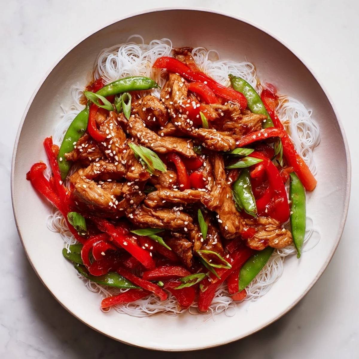 A flavorful bowl of Mongolian Chicken with Rice Noodles, featuring glistening sauce and sesame seeds.
