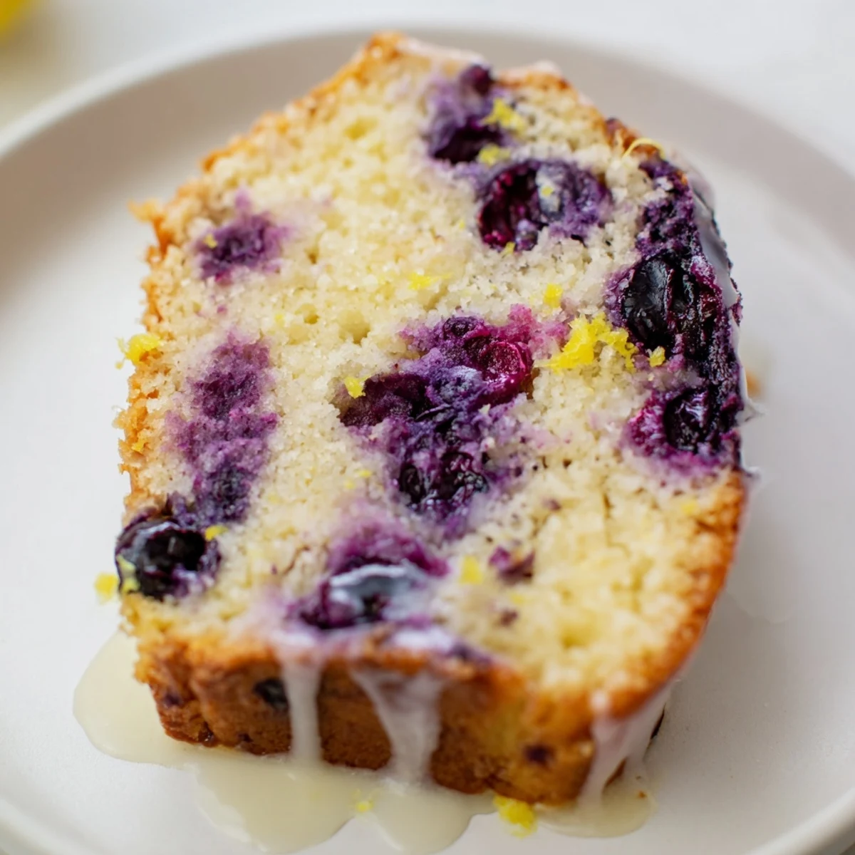 A slice of homemade Lemon Blueberry Yogurt Loaf with a glistening glaze, perfect for a sunny breakfast.