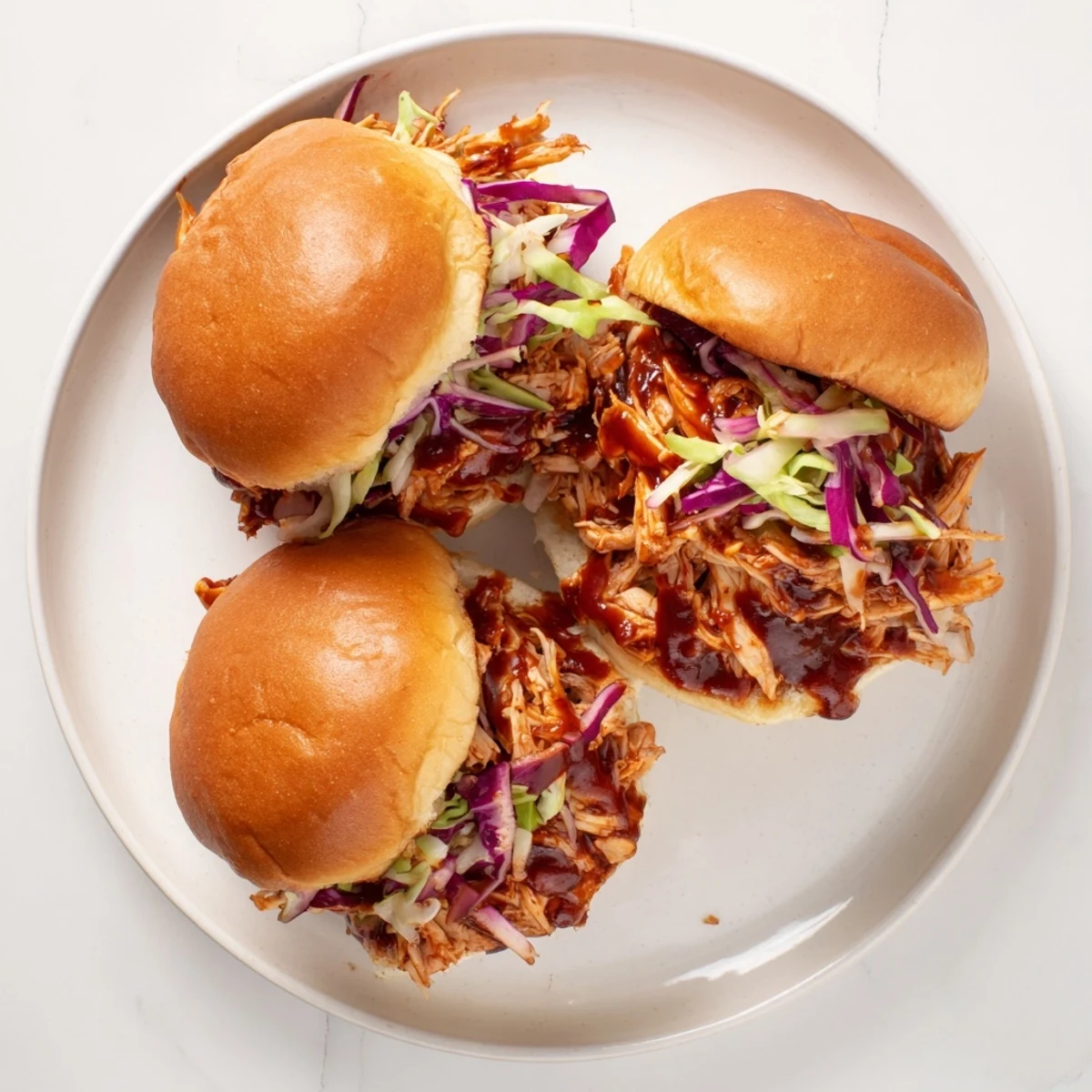 Golden BBQ chicken sliders with crunchy slaw on toasted mini buns, served on a rustic wooden board.