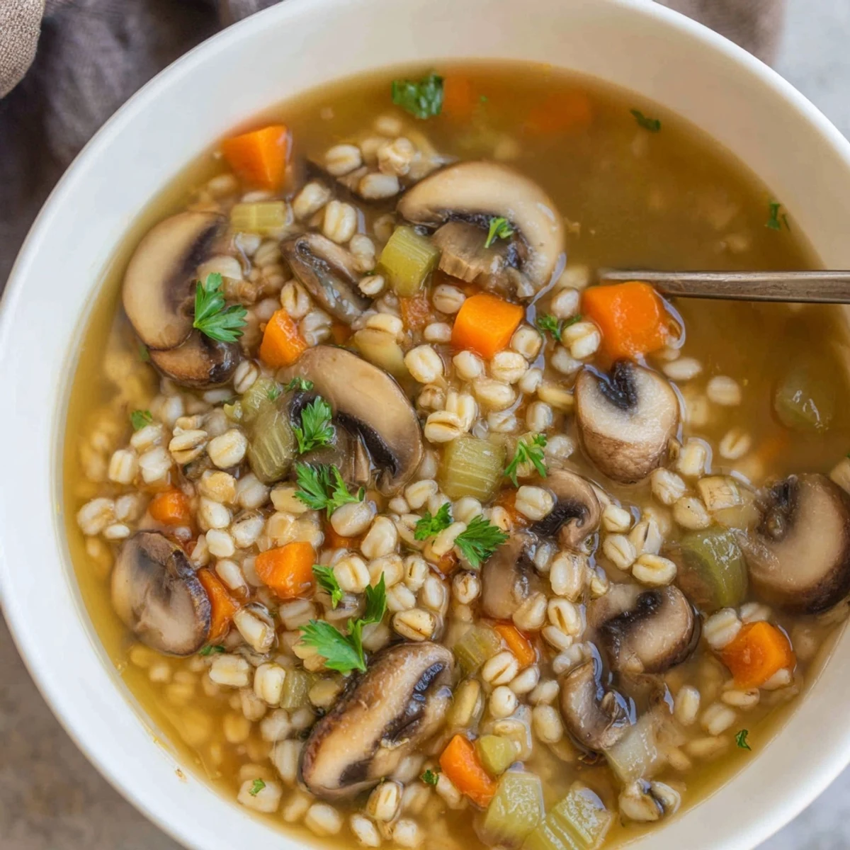A warm bowl of Mushroom and Barley Soup, featuring tender sliced mushrooms and chewy pearl barley in a hearty, golden vegetable broth.