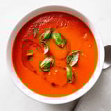 Creamy Tomato and Basil Soup served hot in a rustic bowl with a grilled cheese sandwich on the side.