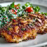 A plated serving of almond-crusted chicken with fresh kale, sumac, and slivered almonds.