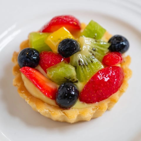 Vibrant mini fruit tartlets showcasing a colorful arrangement of fresh berries and kiwi on top a pastry cream filling.