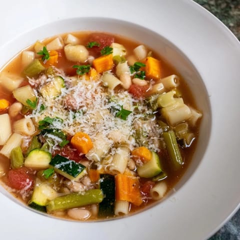 Hearty minestrone vegetable soup in a white bowl, topped with grated Parmesan and fresh basil, served with crusty bread.