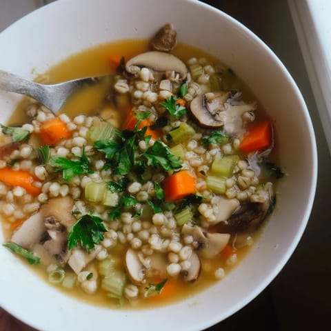 Close-up view of Mushroom and Barley Soup in a rustic bowl, garnished with fresh parsley and a hint of lemon for brightness.