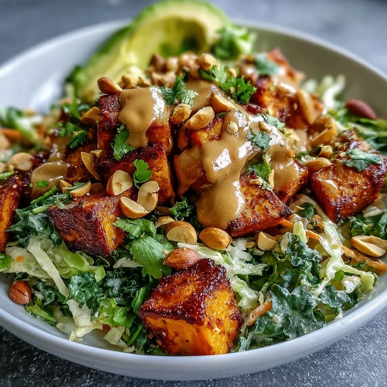 Vibrant plant-based Thai Peanut Sweet Potato Buddha Bowl drizzled with sauce, featuring broccoli, carrots, and fresh garnishes.
